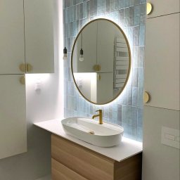 OPTIMA SKY - Stylowa łazienka z owalnym lustrem podświetlanym LED, umywalką nablatową i błękitnymi płytkami ułożonymi pionowo. Złote akcenty armatury i oświetlenia.