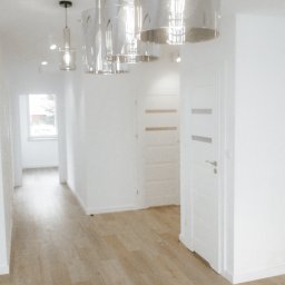 OPTIMA SKY - Jasne wnętrze po remoncie w Gdańsku: drewnopodobne panele, białe ściany i drzwi, nowoczesne lampy wiszące. Minimalistyczny design, czystość i porządek.