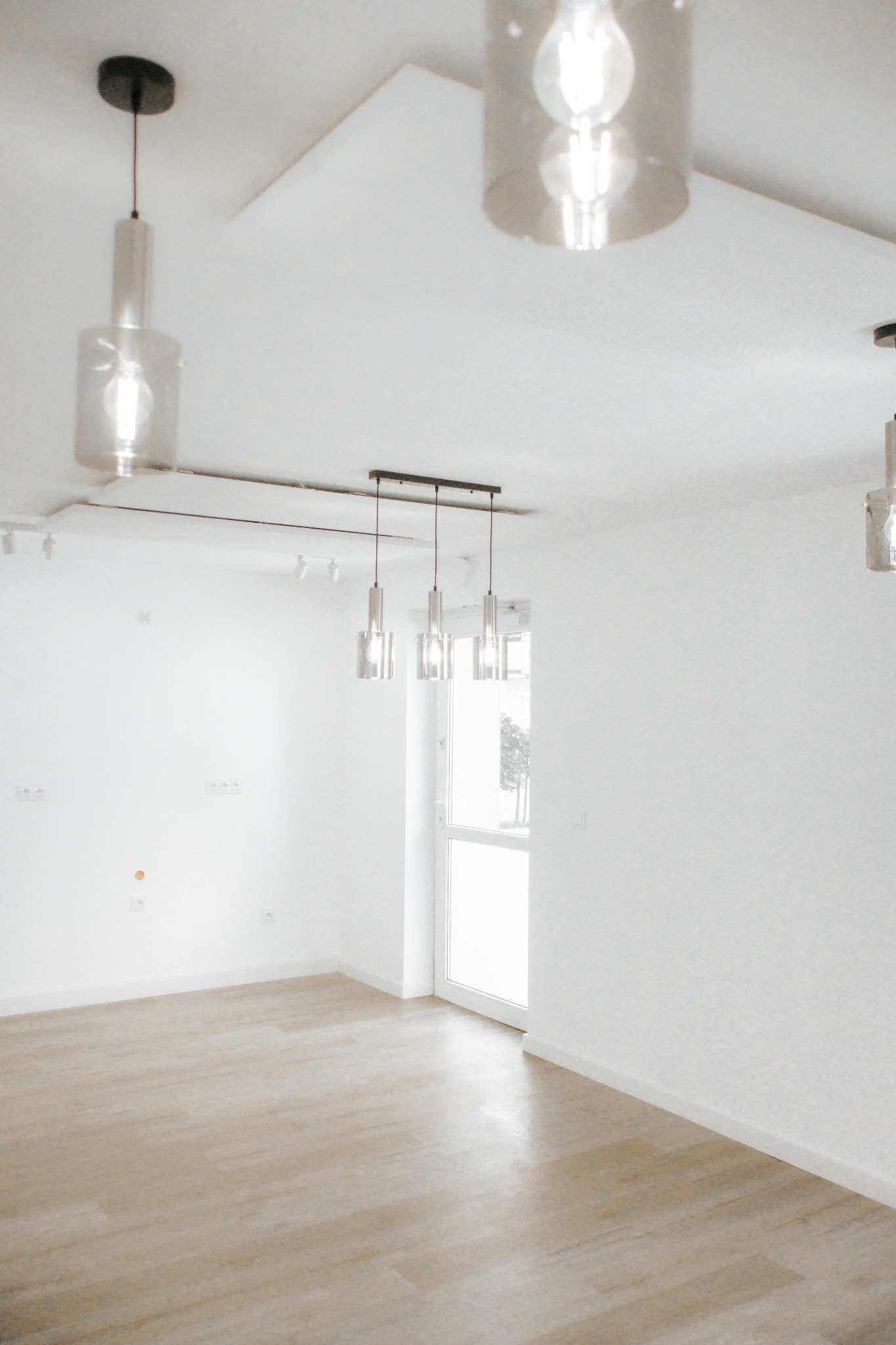 Jasne wnętrze po remoncie: panele podłogowe, białe ściany z widocznymi gniazdkami, nowoczesne lampy wiszące. Minimalistyczny design, naturalne światło.