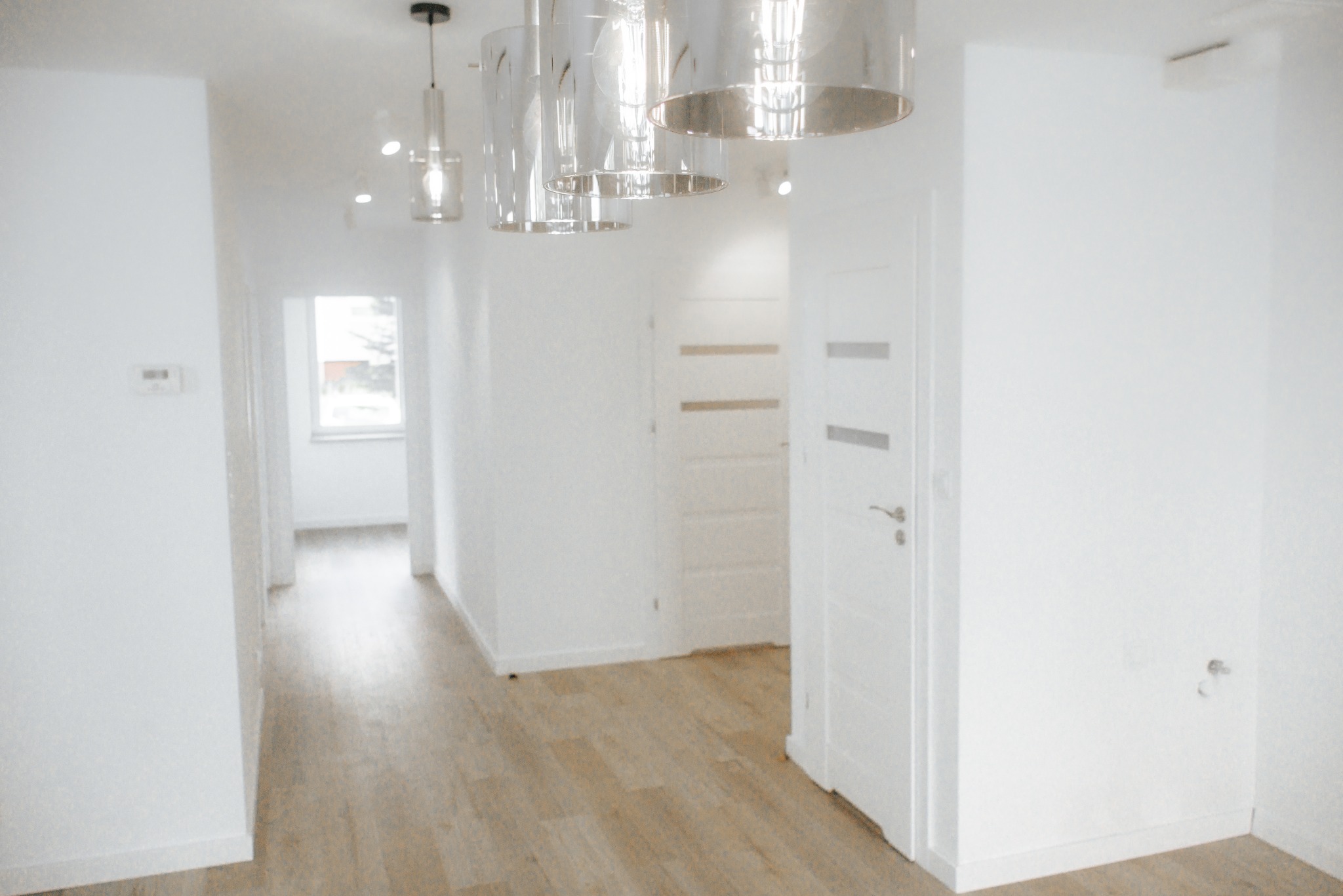 Jasne wnętrze po remoncie w Gdańsku: drewnopodobne panele, białe ściany i drzwi, nowoczesne lampy wiszące. Minimalistyczny design, czystość i porządek.