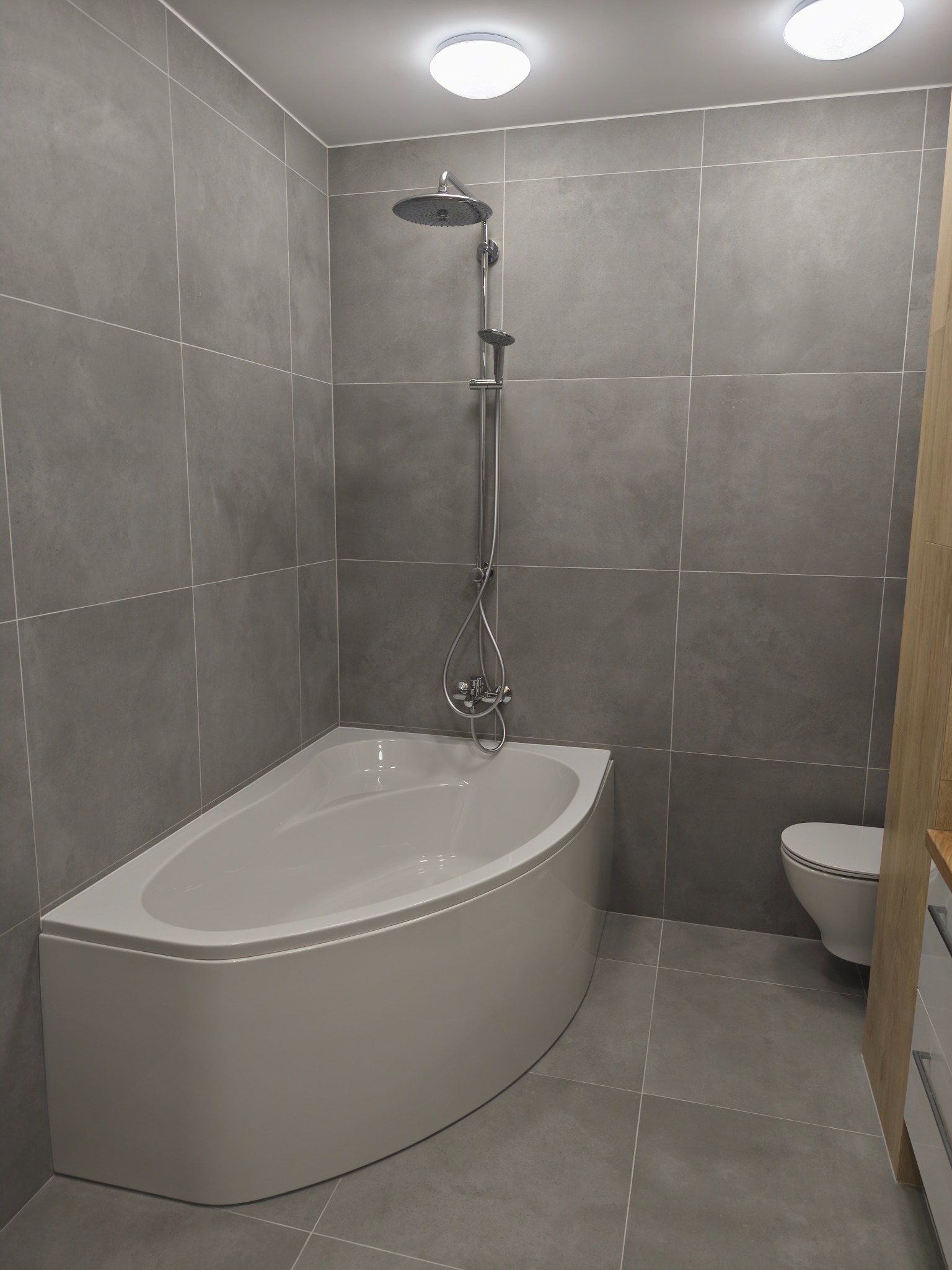 Nowoczesna łazienka z szarymi płytkami, białą wanną narożną i toaletą. Minimalistyczny design, oświetlenie sufitowe. Widok na kabinę prysznicową.