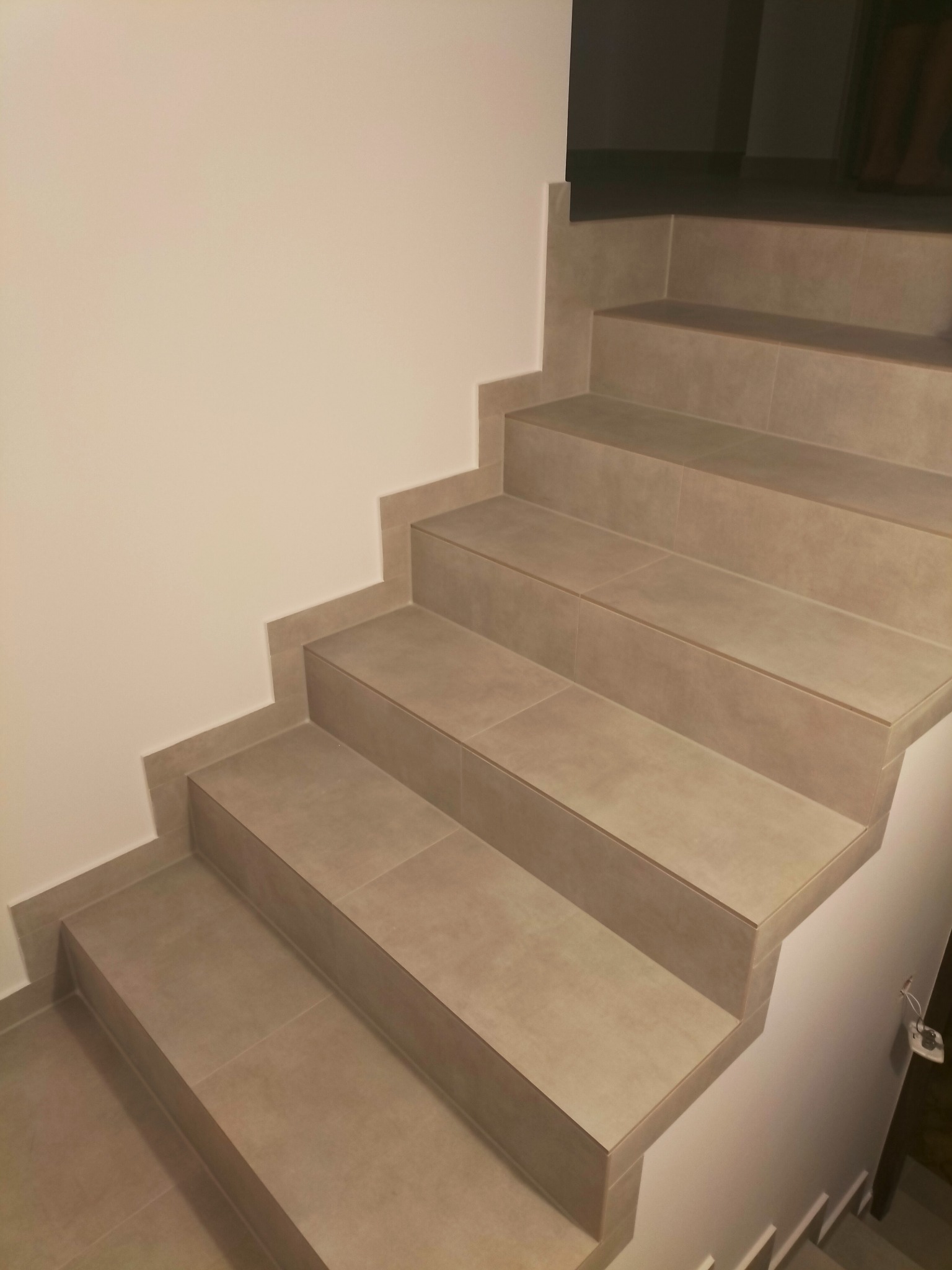 Schody wykończone płytkami ceramicznymi w odcieniach beżu, widok z dołu, jasne ściany, minimalistyczny design.