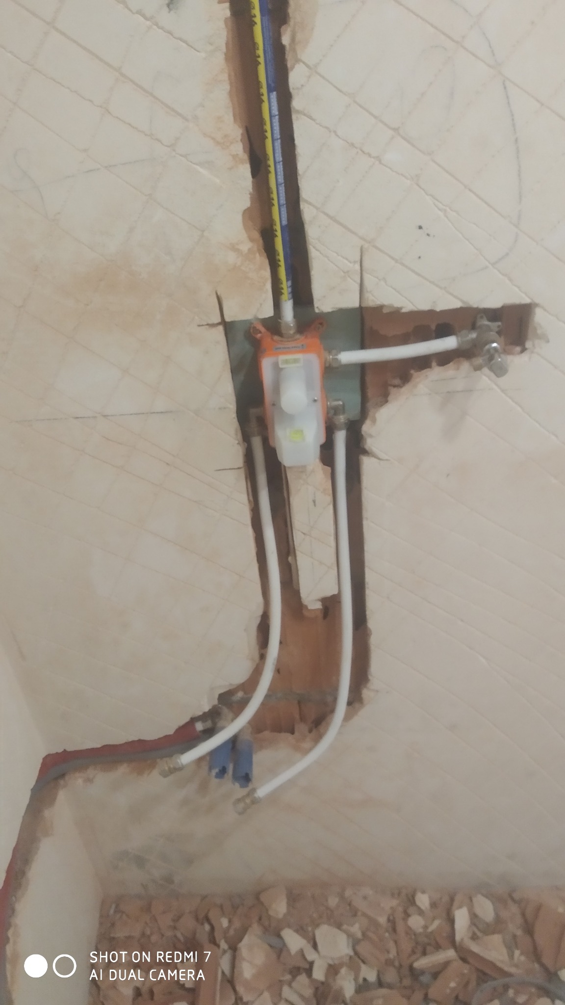 Wnęka w ścianie z widoczną instalacją wodną podczas prac remontowych, z fragmentami gruzu na podłodze.