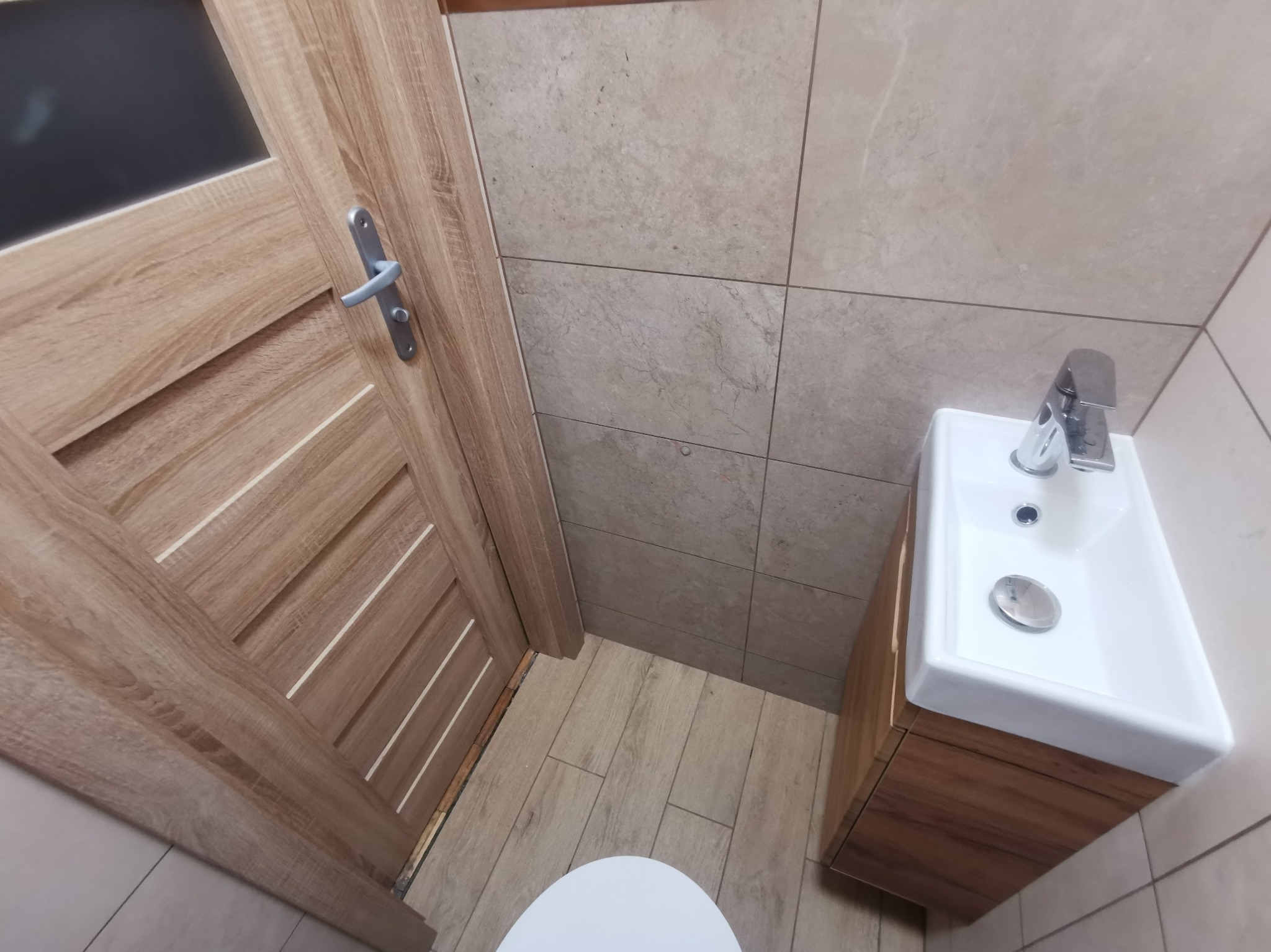 Wykończona łazienka we Wrocławiu z drewnopodobnymi płytkami na podłodze i ścianach, widoczna umywalka z szafką i fragment drzwi.