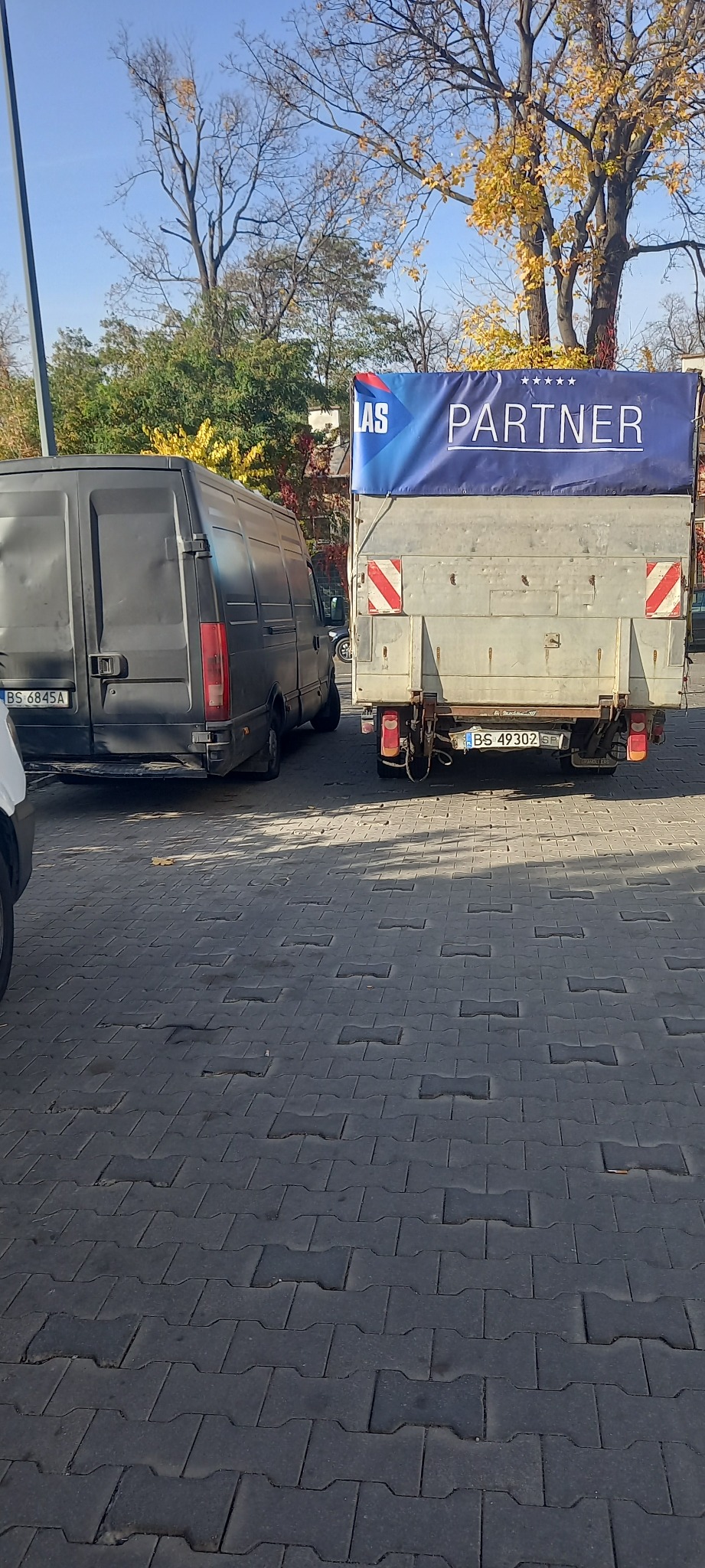 Dwa busy zaparkowane na brukowanej ulicy, jeden z plandeką reklamową z napisem PARTNER, widok z tyłu.