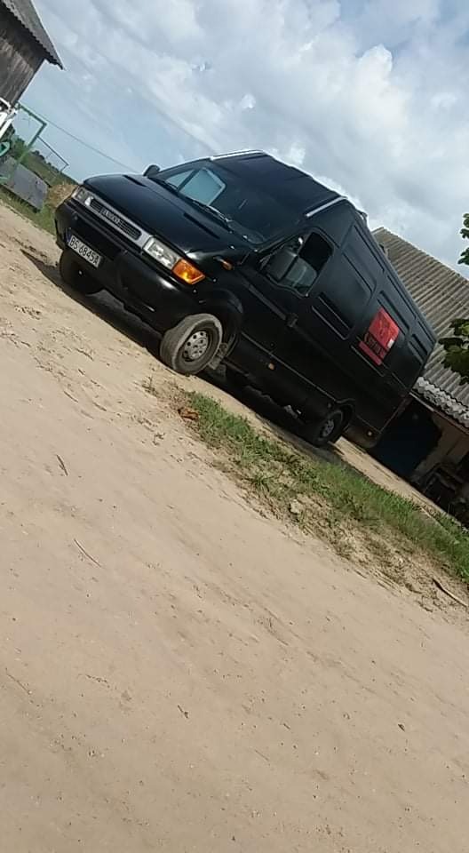 Czarny bus transportowy marki Iveco Daily zaparkowany na piaszczystej drodze wiejskiej, widok z boku, pochmurne niebo.