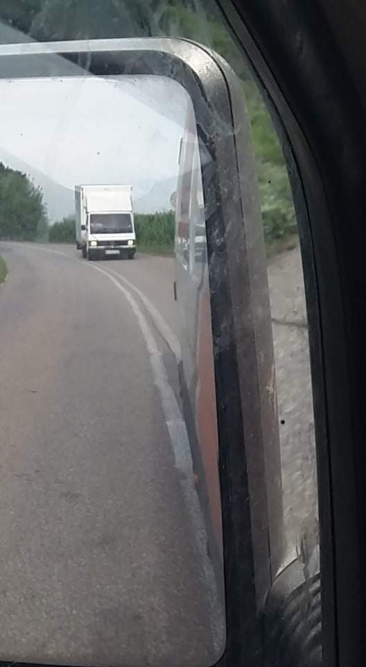 Widok w lusterku bocznym samochodu na białą furgonetkę jadącą po asfaltowej drodze w pochmurny dzień.