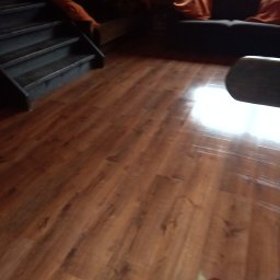 Maciej ALFUTH - Nowa podłoga drewnopodobna w salonie z ciemnymi schodami i sofą. Widoczne ślady po lakierowaniu na powierzchni.