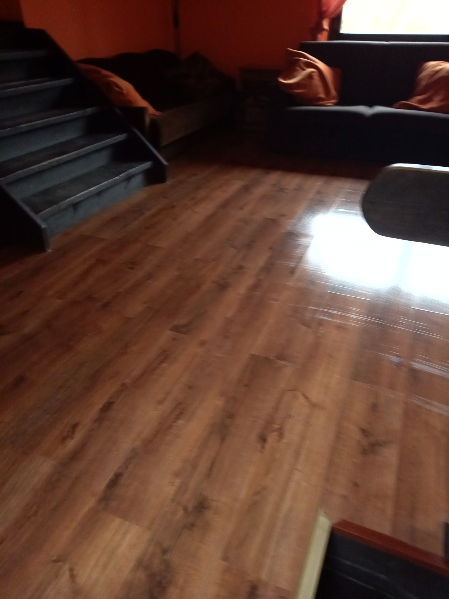 Nowa podłoga drewnopodobna w salonie z ciemnymi schodami i sofą. Widoczne ślady po lakierowaniu na powierzchni.