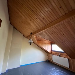 Artur Solo - Poddasze zabezpieczone folią malarską przed malowaniem ścian, widoczny grzejnik i drewniana boazeria na suficie oraz okno dachowe.