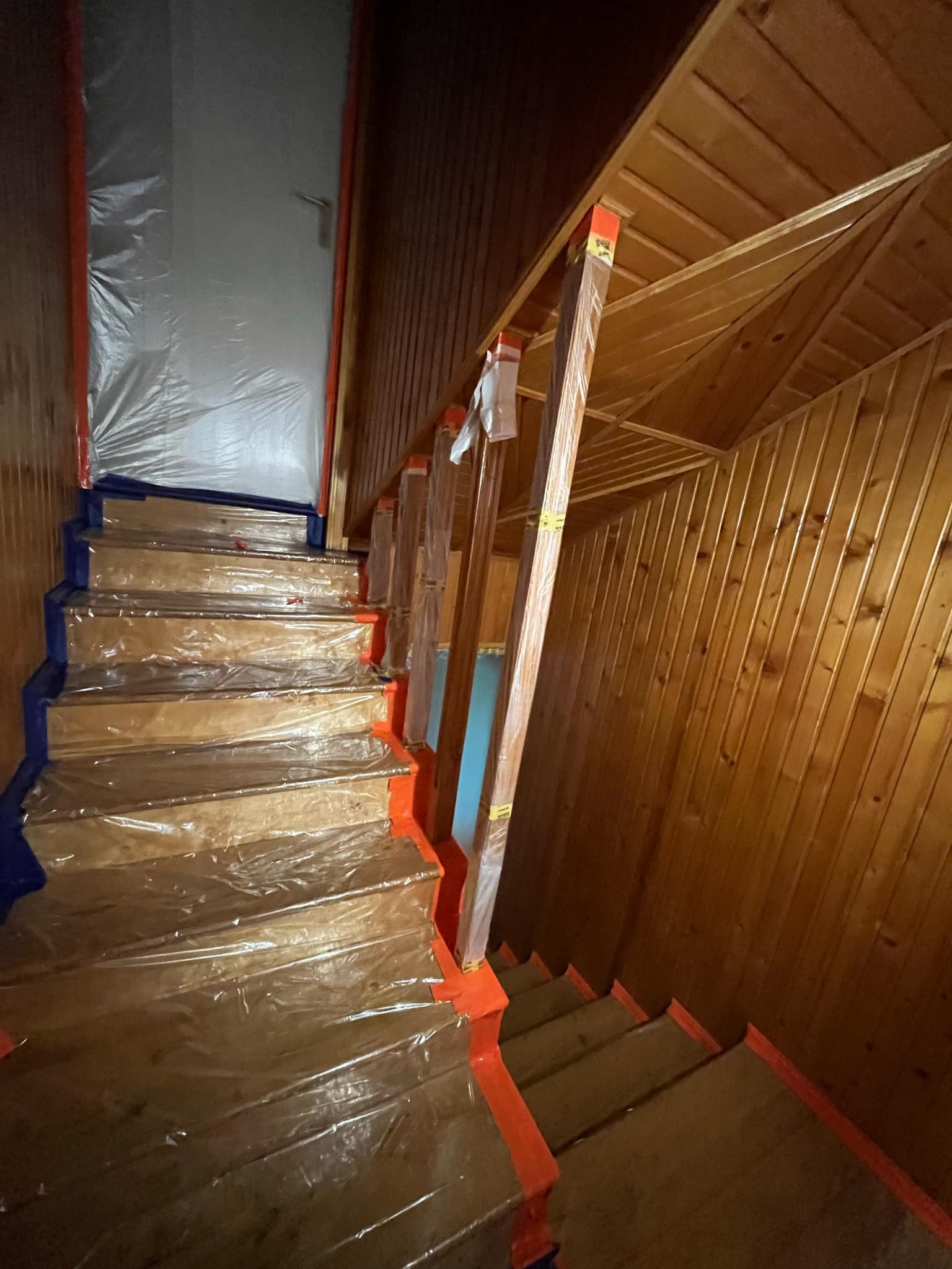 Schody drewniane zabezpieczone folią i taśmą malarską przed malowaniem, ściany i sufit wyłożone boazerią.