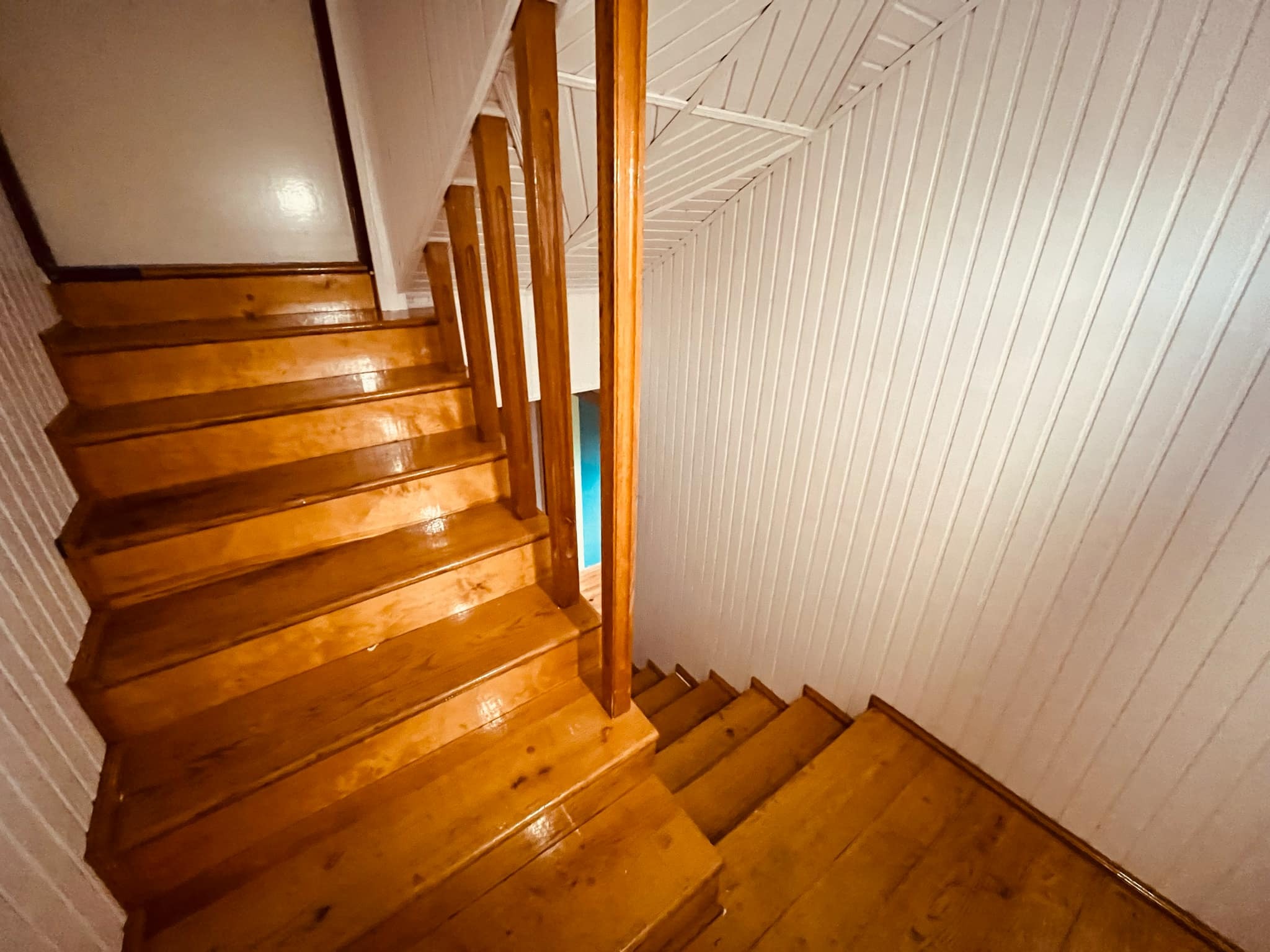 Odnowione drewniane schody z lakierowanymi stopniami i pomalowaną na biało boazerią ścienną, widok z góry na dół.