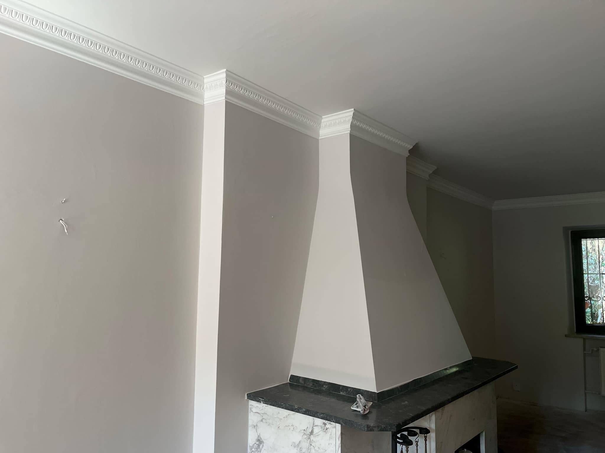 Jasnoszare wnętrze po malowaniu z ozdobnymi białymi listwami przysufitowymi i kominkiem obudowanym marmurem.