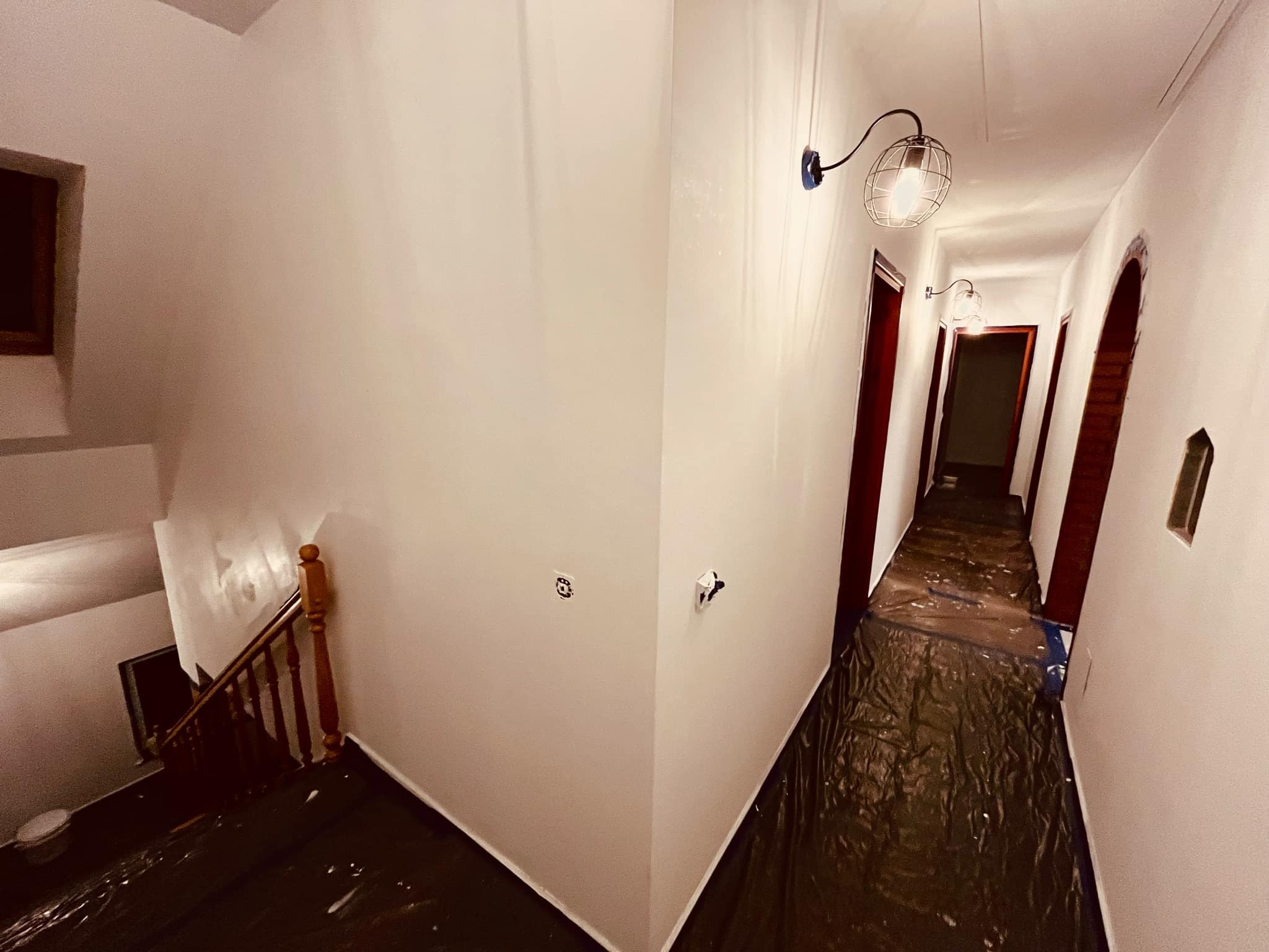 Korytarz i schody zabezpieczone folią malarską, ściany świeżo pomalowane na biało, widoczne lampy w stylu industrialnym.
