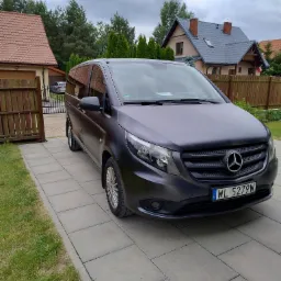 Szary Mercedes Vito, zaparkowany na posesji z kostki brukowej. W tle domy jednorodzinne i ogrodzenie. Tablica rejestracyjna z Warszawy.