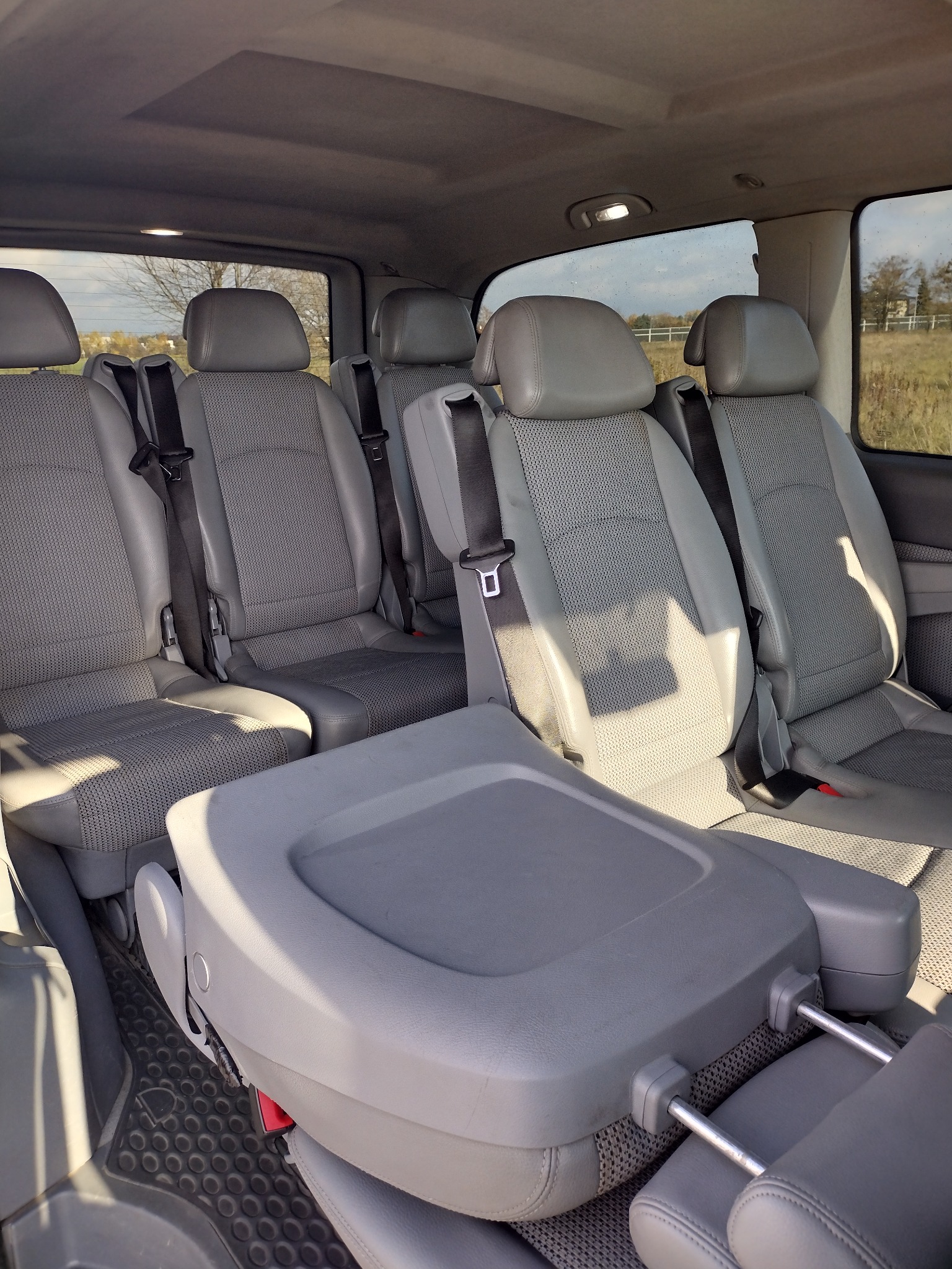 Wnętrze przestronnego busa z szarymi, regulowanymi fotelami pasażerskimi i widokiem na krajobraz za oknem.