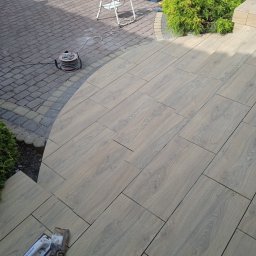 Bartłomiej Błaszkowski - Ułożona, drewnopodobna terakota na schodach i tarasie w Sułkowicach, widoczne narzędzia glazurnicze i zwinięty przedłużacz, w tle drabina i skrzynka narzędziowa.