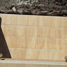 Bartłomiej Błaszkowski - Układanie płytek imitujących drewno na balkonie, widoczny fragment buta roboczego i przygotowane podłoże.