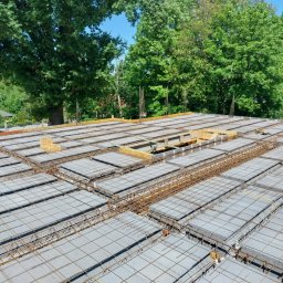 Wojtek - Wieniec stropowy Teriva w trakcie budowy, widoczne zbrojenie i betonowe pustaki stropowe, w tle zieleń drzew.