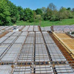 Wojtek - Zbrojenie stropu Teriva z pustakami betonowymi, widok z góry na siatkę zbrojeniową i drewniane szalunki, w tle zieleń drzew i budynek gospodarczy.