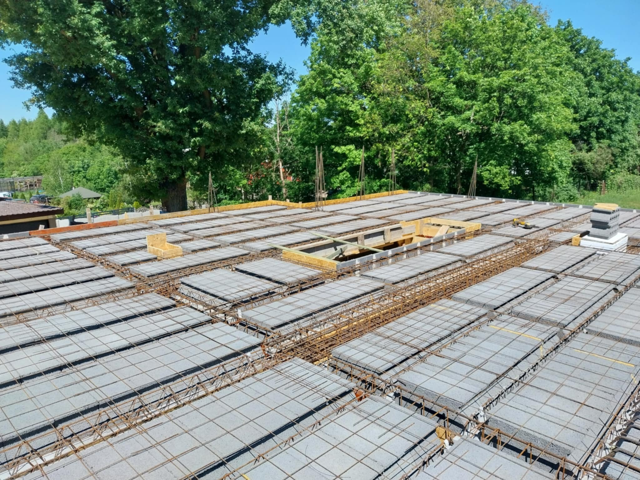 Wieniec stropowy Teriva w trakcie budowy, widoczne zbrojenie i betonowe pustaki stropowe, w tle zieleń drzew.