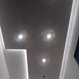 Sufit podwieszany z szarą powierzchnią i punktowymi źródłami światła oraz liniowym oświetleniem LED w narożniku.