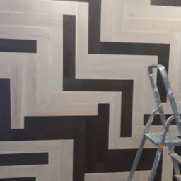 Dwukolorowy parkiet ułożony we wzór jodełki francuskiej, z widocznymi elementami drabiny malarskiej i akcesoriami montażowymi na podłodze.