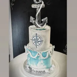 Dwupoziomowy tort z motywem morskim, zdobiony srebrnym kotwicą, kompasem i napisem '18 FABIANA' na tle czarnej tablicy z dekoracjami.