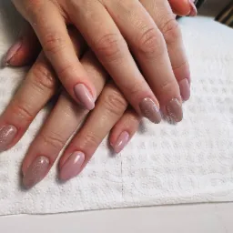 Dłonie z różnymi odcieniami lakieru, jeden z brokatem, na tle białej serwetki i lampy UV do utwardzania lakieru hybrydowego.