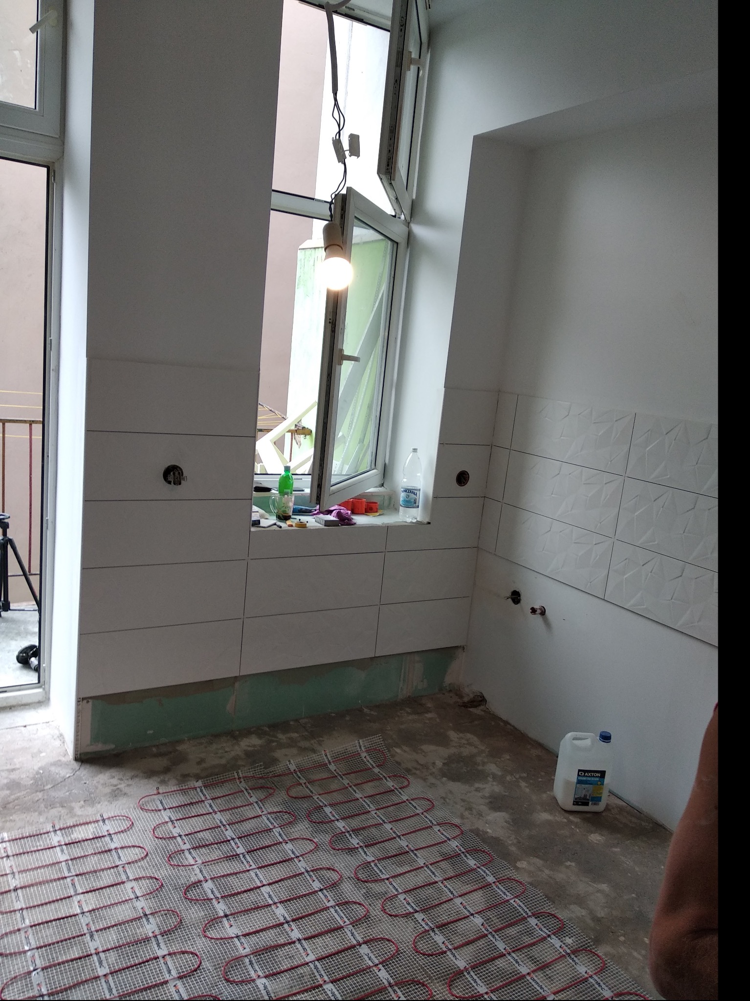 Montaż ogrzewania podłogowego elektrycznego w trakcie remontu mieszkania, widoczne płytki ścienne, okno i materiały budowlane.