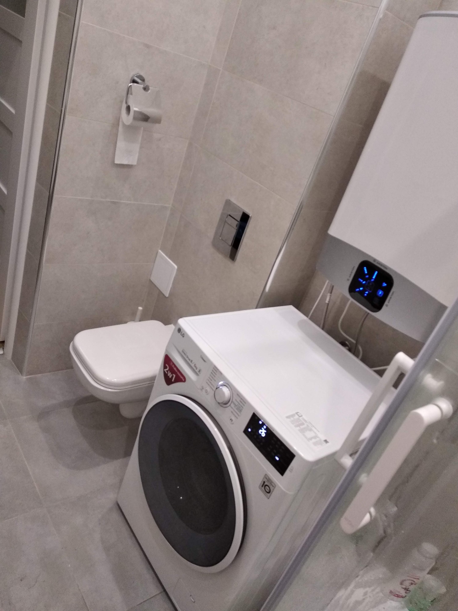 Wnętrze łazienki z pralką LG, toaletą i grzejnikiem wody, wykończone płytkami w odcieniach szarości.