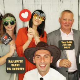 Grupa uśmiechniętych osób w przebraniach i z rekwizytami pozuje do zdjęcia na tle drewnianej ścianki.