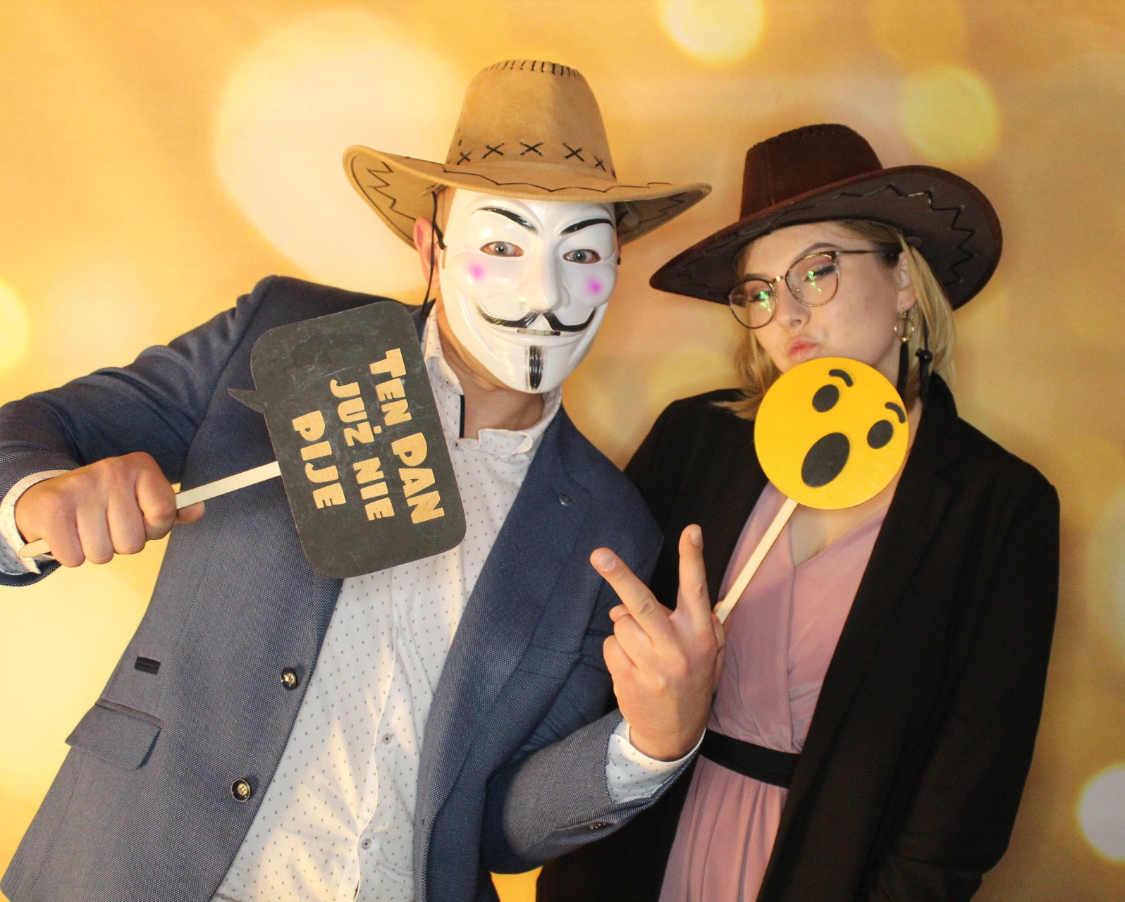 Dwie osoby w przebraniach pozują z rekwizytami przed tłem w Gorzowie Wielkopolskim. Mężczyzna w masce i kapeluszu kowbojskim trzyma tabliczkę z napisem 'Ten Pan już nie pije', a kobieta z okularami...