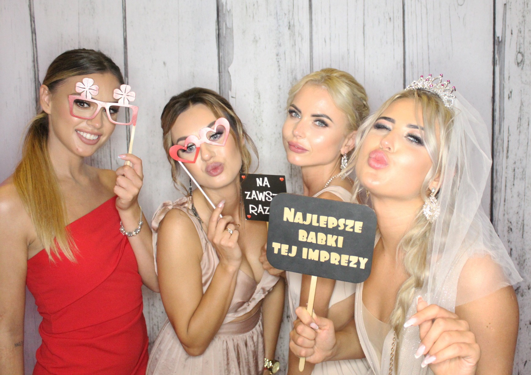 Cztery uśmiechnięte kobiety pozują z rekwizytami (okulary z kwiatkami, serduszka) i tabliczkami z napisami 'Na zawsze raz' i 'Najlepsze babki tej imprezy' na tle jasnej ściany.