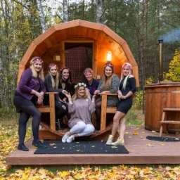 Grupa kobiet w wiankach pozuje przed drewnianą sauną beczką i balią w plenerze w okolicy Białegostoku, jesienne liście na ziemi.