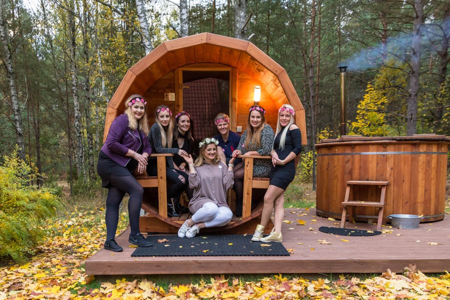 Grupa kobiet w wiankach pozuje przed drewnianą sauną beczką i balią w plenerze w okolicy Białegostoku, jesienne liście na ziemi.