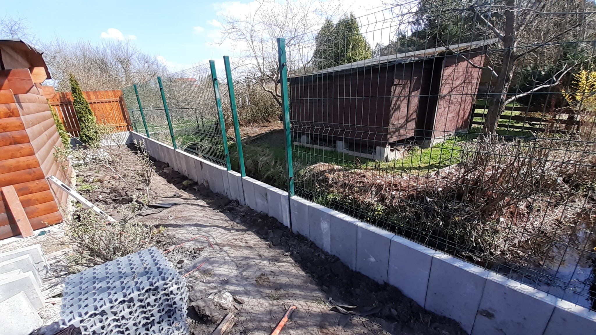 Świeżo postawiony, szary, betonowy murek pod ogrodzenie panelowe z zielonymi słupkami, widok z góry na teren działki z drewnianą altaną w tle.