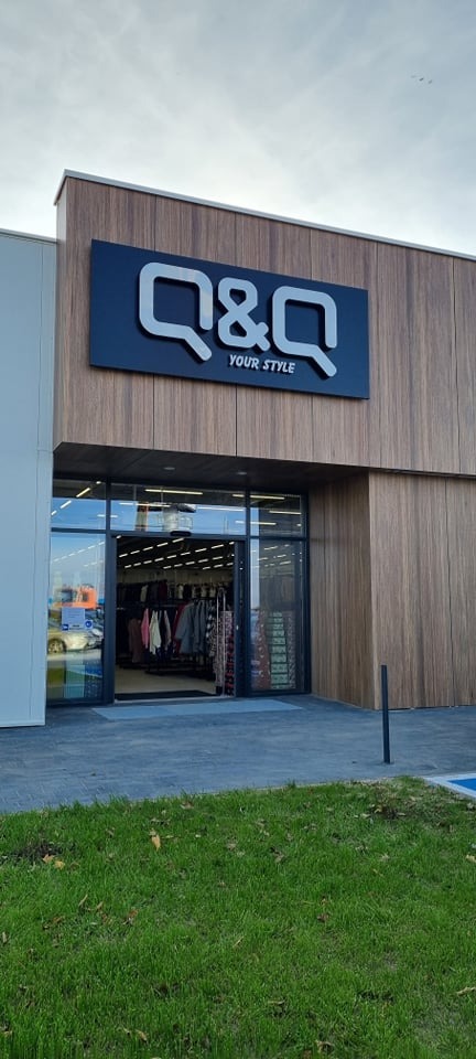 Fasada sklepu odzieżowego z dużym szyldem 'Q&Q YOUR STYLE' nad wejściem, widoczne ubrania na wieszakach wewnątrz.