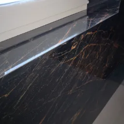 Błyszczący, czarny blat z marmurkowym wzorem w odcieniach złota, przylegający do białego okna PCV. Widoczne odbicie światła na powierzchni blatu.