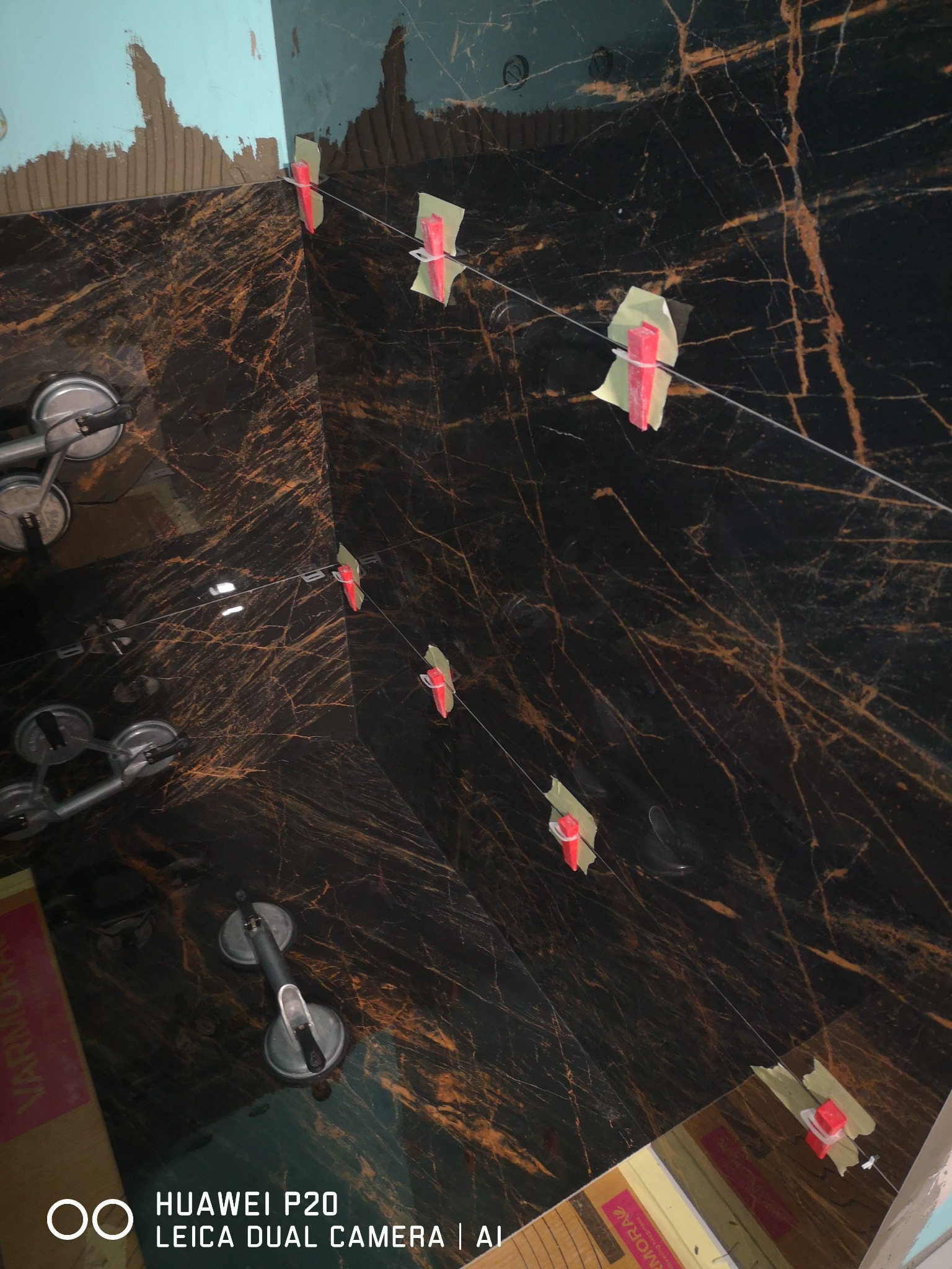 Ułożone płytki imitujące marmur z widocznymi przyssawkami do przenoszenia i systemem poziomowania płytek (klipsy i kliny) w trakcie prac wykończeniowych.