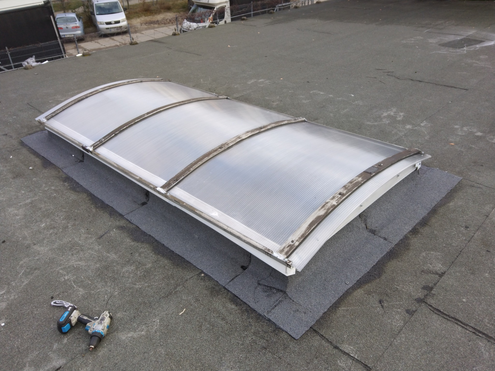 Płaski dach pokryty papą z zamontowanym świetlikiem dachowym, obok leży wkrętarka akumulatorowa.