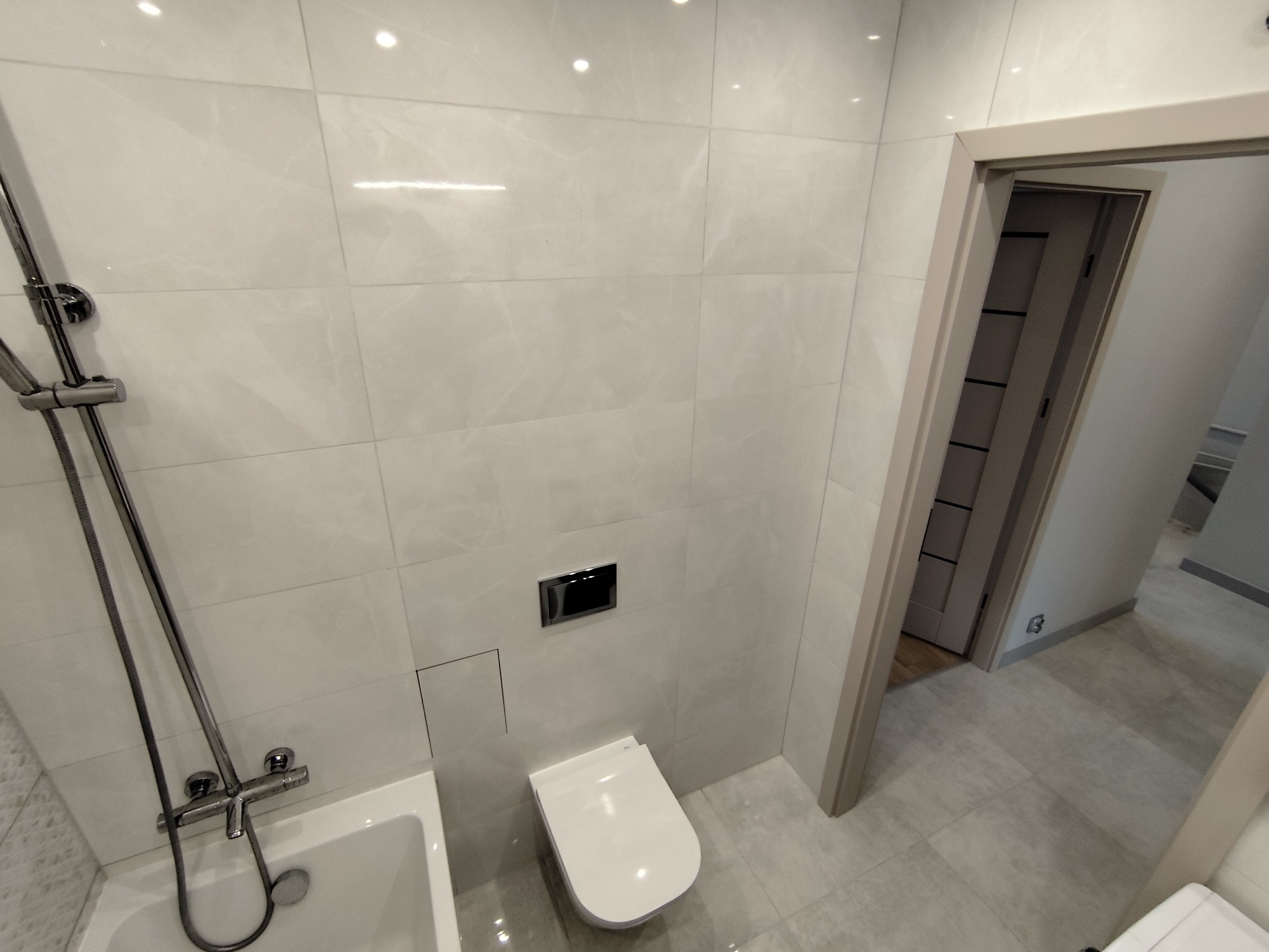 Jasna łazienka po remoncie: białe płytki imitujące marmur na ścianach, podwieszana toaleta, chromowana armatura i widok na drzwi wewnętrzne.