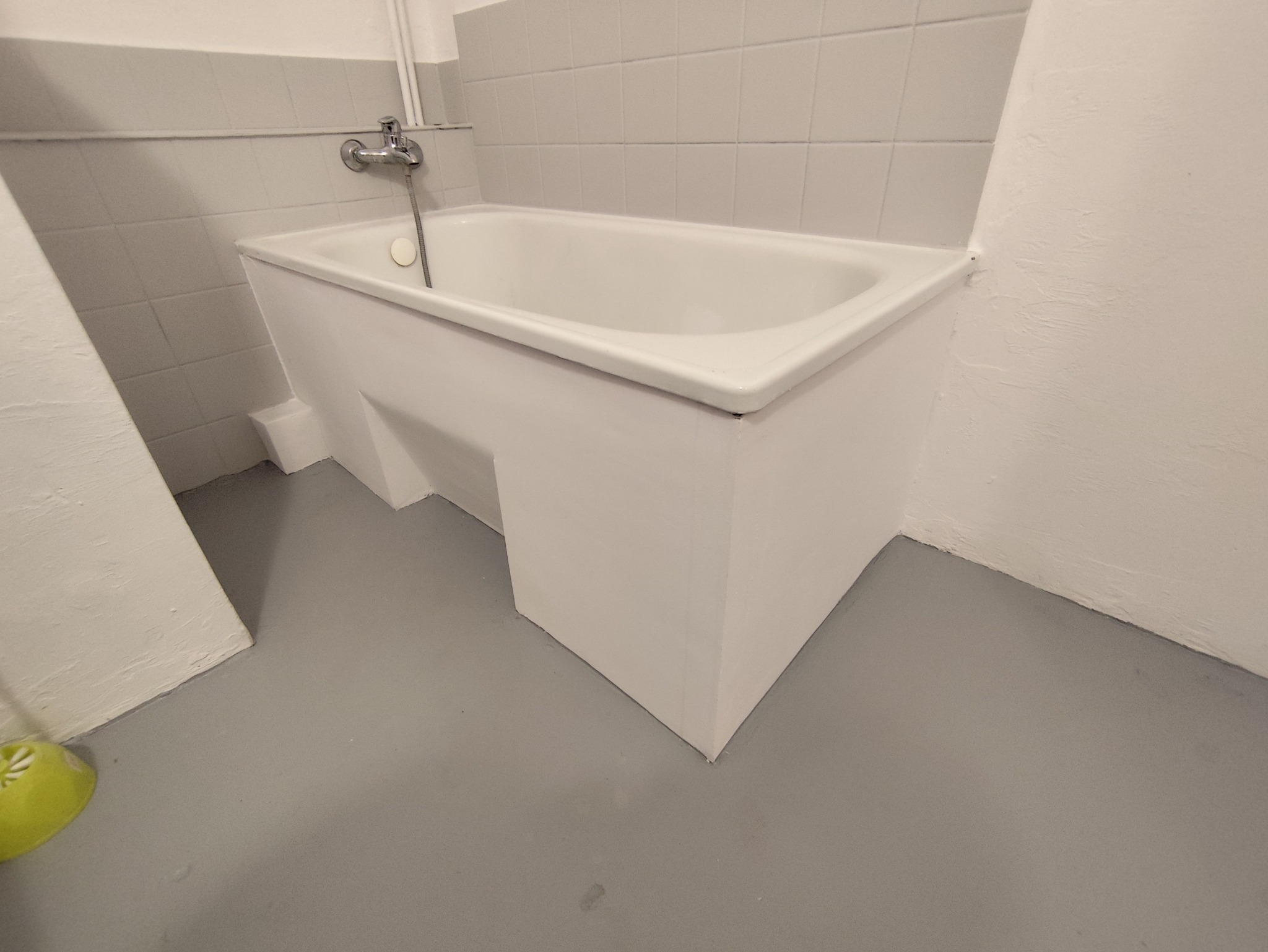 Biała wanna z zabudową w wykafelkowanej łazience po remoncie. Widoczna bateria i szare płytki podłogowe. Minimalistyczny design.