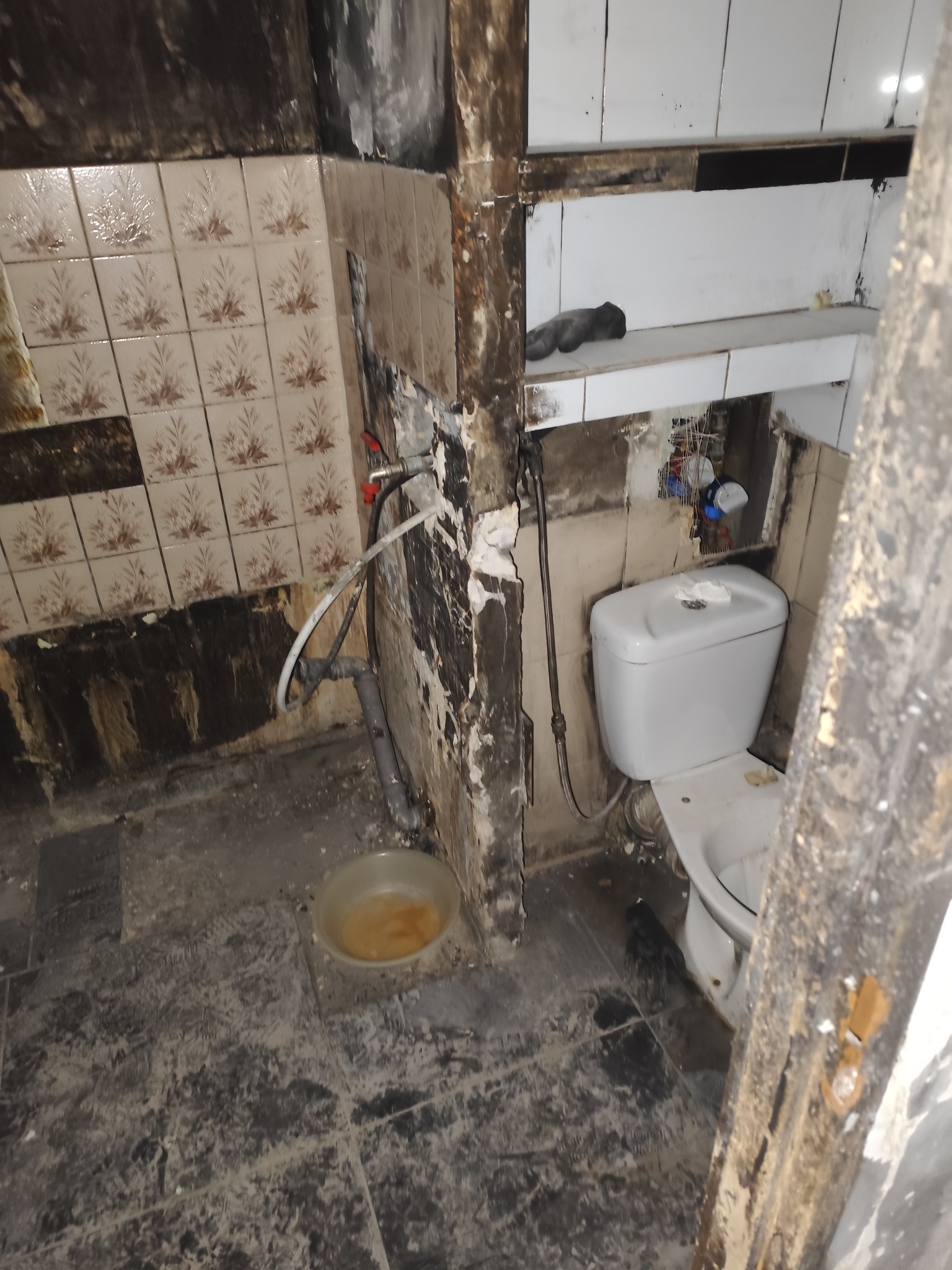 Zdemolowana łazienka w trakcie prac. Widoczne stare płytki, instalacje, toaleta i ślady po demontażu. Przygotowanie do remontu, widok z góry.