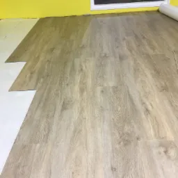 Fragment podłogi z paneli w trakcie układania, widoczny podkład i żółta ściana w tle.