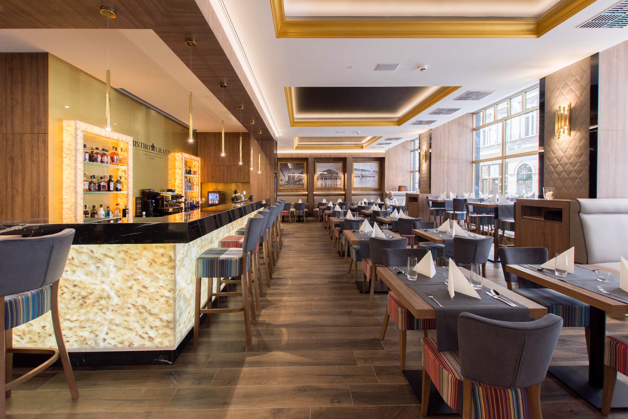 Eleganckie wnętrze restauracji z podświetlanym barem z onyksu, szarymi krzesłami barowymi i stolikami nakrytymi szarymi bieżnikami, widok na okna z widokiem na miasto.
