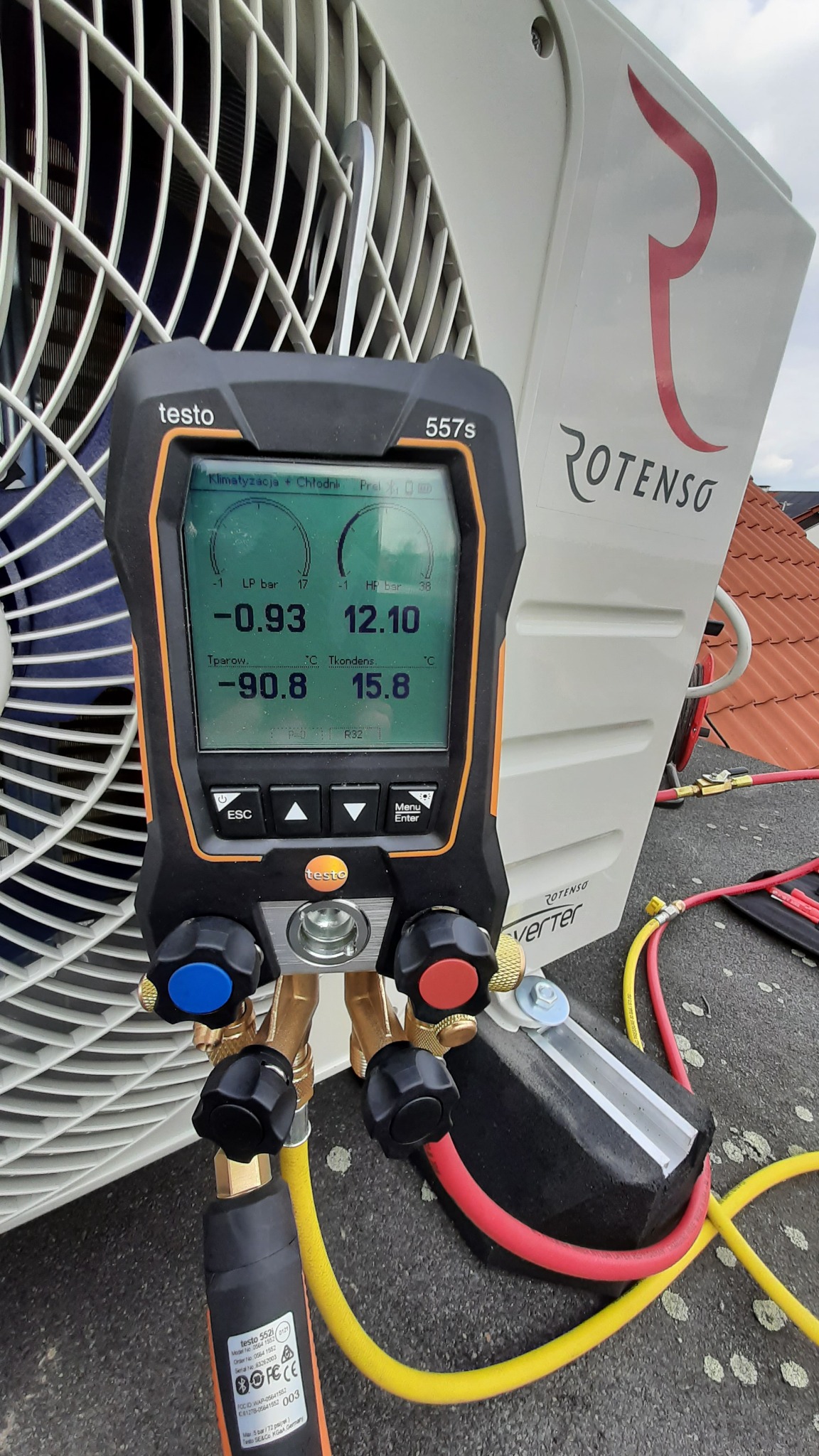 Pomiar ciśnienia i temperatury klimatyzacji na dachu za pomocą cyfrowego kolektora Testo 557s, widoczny wentylator jednostki zewnętrznej i logo Rotenso.