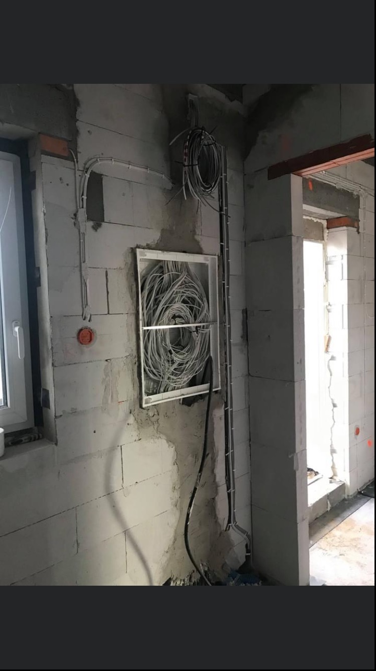 Surowy mur z widocznymi przewodami elektrycznymi w puszce instalacyjnej i na powierzchni ściany, instalacja w trakcie realizacji.