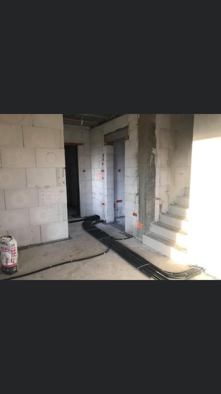 Surowy stan wnętrza w trakcie prac instalacyjnych: widoczne ściany z betonu komórkowego, przygotowane otwory pod gniazdka i wiązka czarnych kabli elektrycznych leżąca na podłodze.