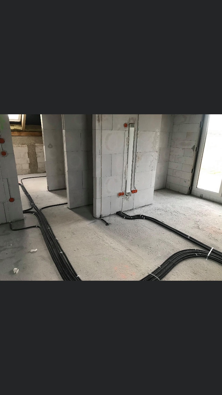 Surowe wnętrze w trakcie prac instalacyjnych: kable elektryczne ułożone w wiązkach na podłodze, puszki instalacyjne w ścianach z betonu komórkowego.